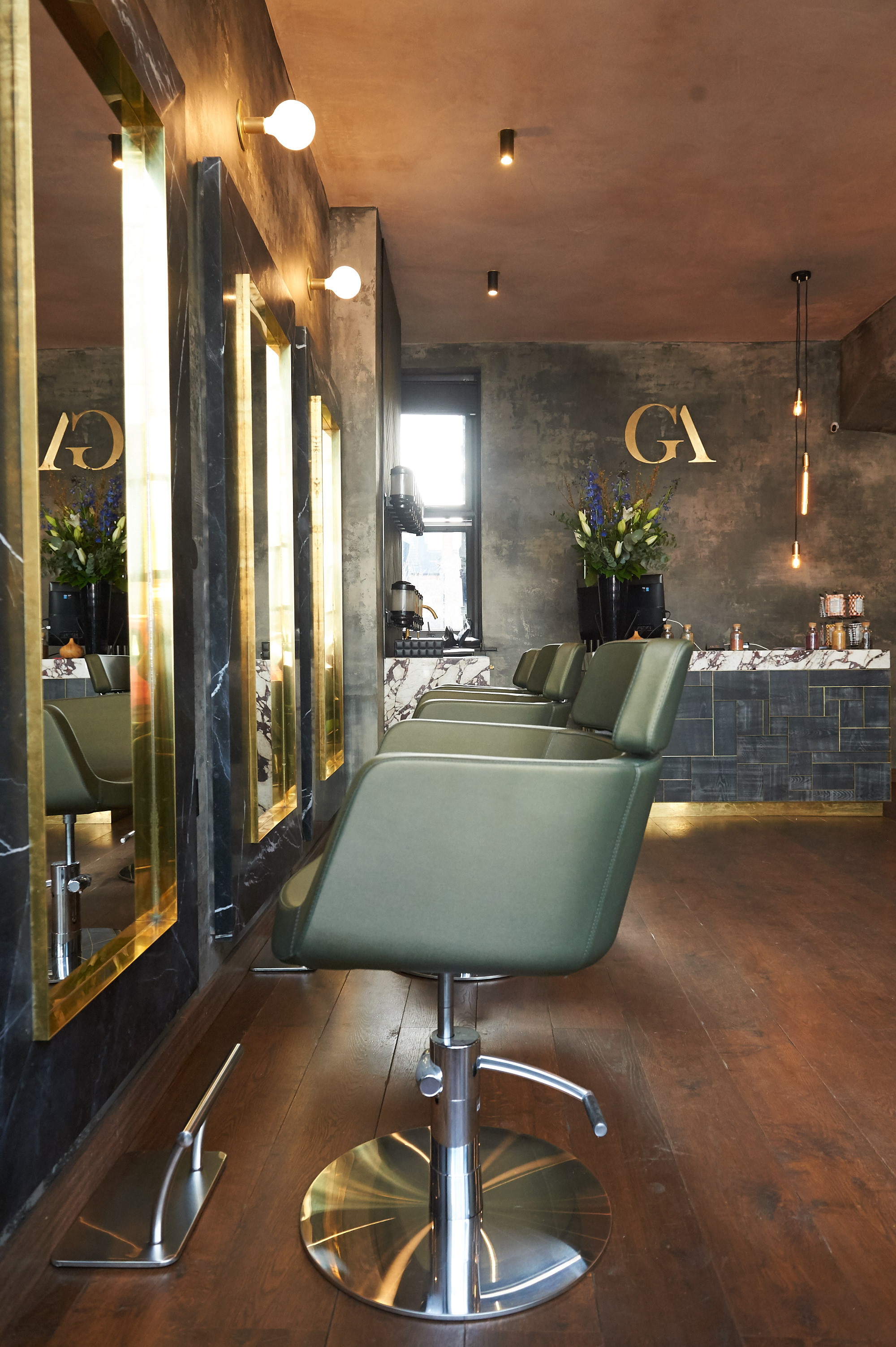 GA Wimbledon styling area with sage green chairs, concrete walls, and professional stations